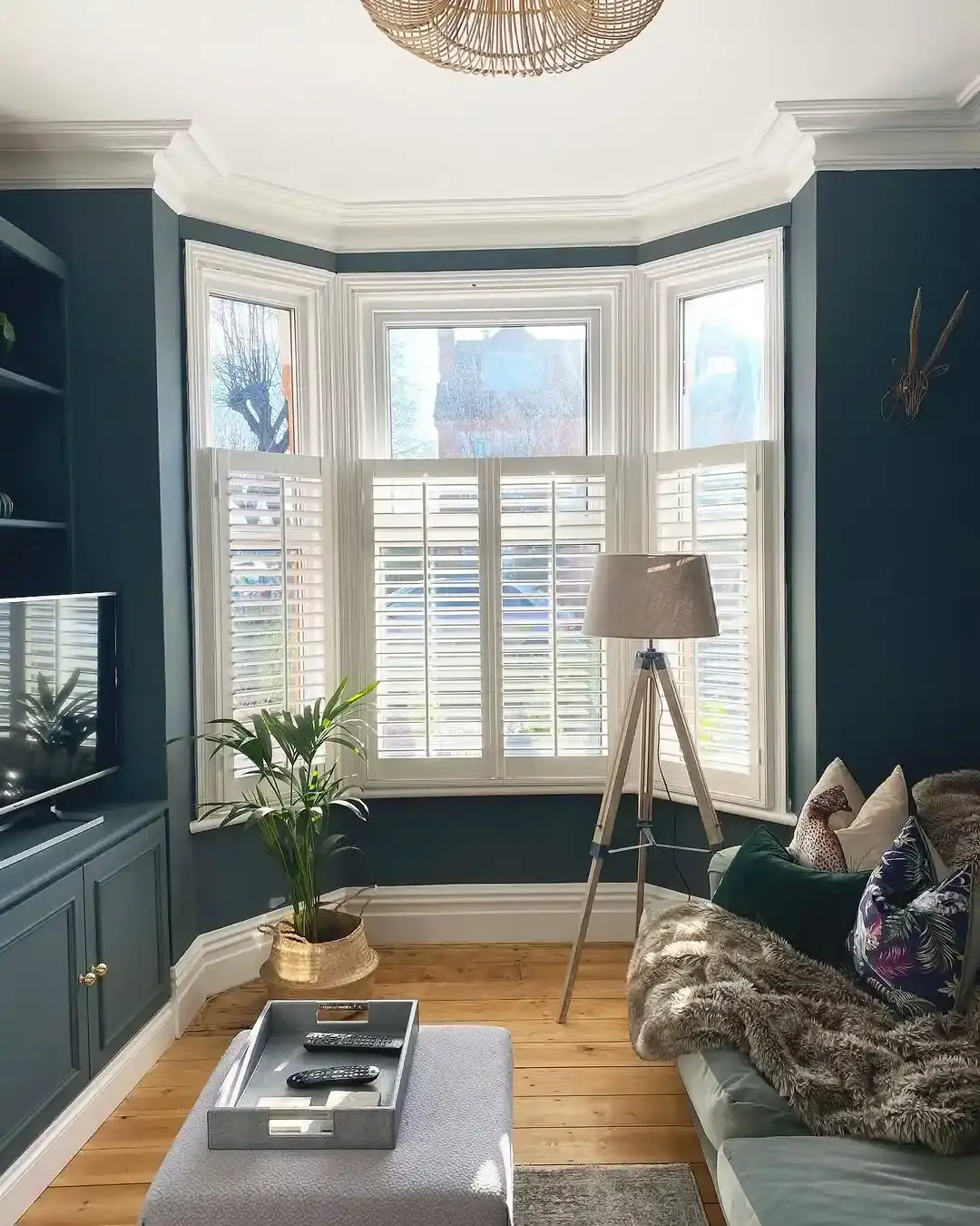 White Cafe Style Shutters with central tilt rod in living room against blue walls and a tripod lamp