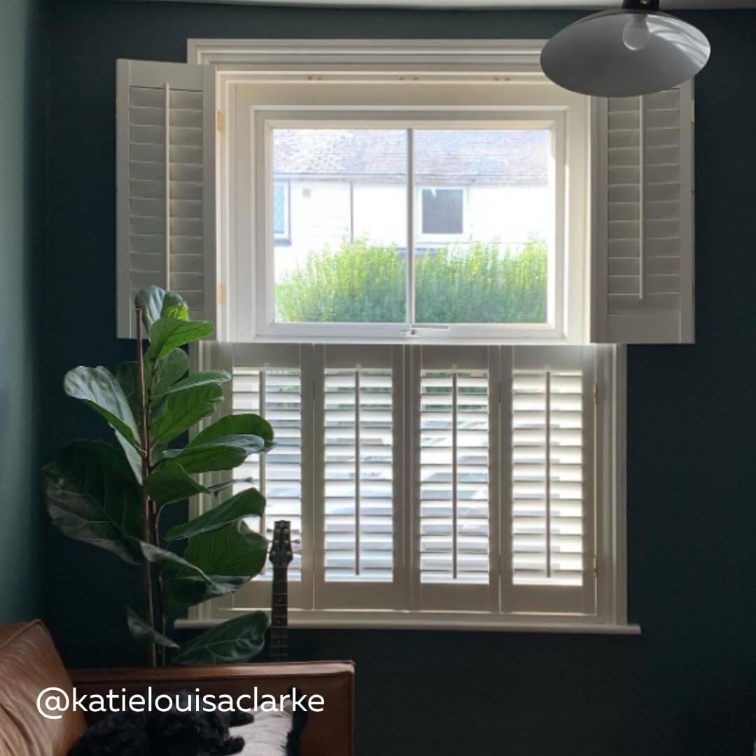 White Tier on Tier Shutters with central tilt rod framed against dark walls. Plus a fiddle leaf fig