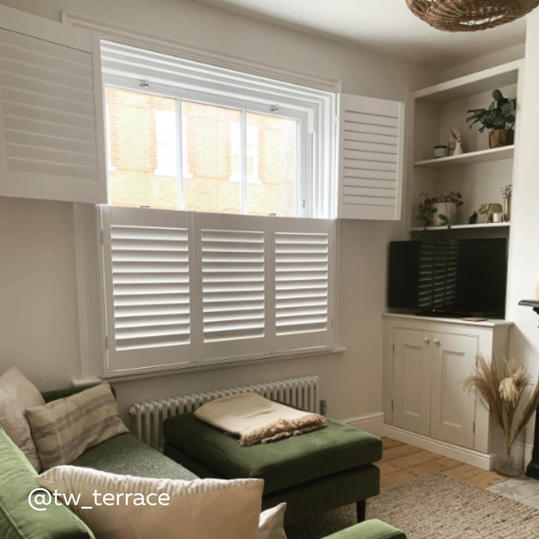 White Tier on Tier Shutters in a cosy living room with green velvet sofa and footrest