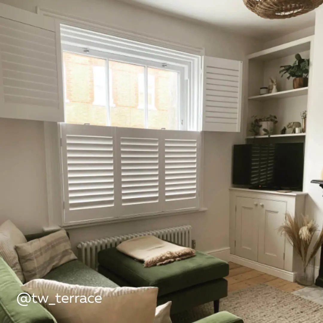 White Tier on Tier Shutters in a cosy living room with green velvet sofa and footrest