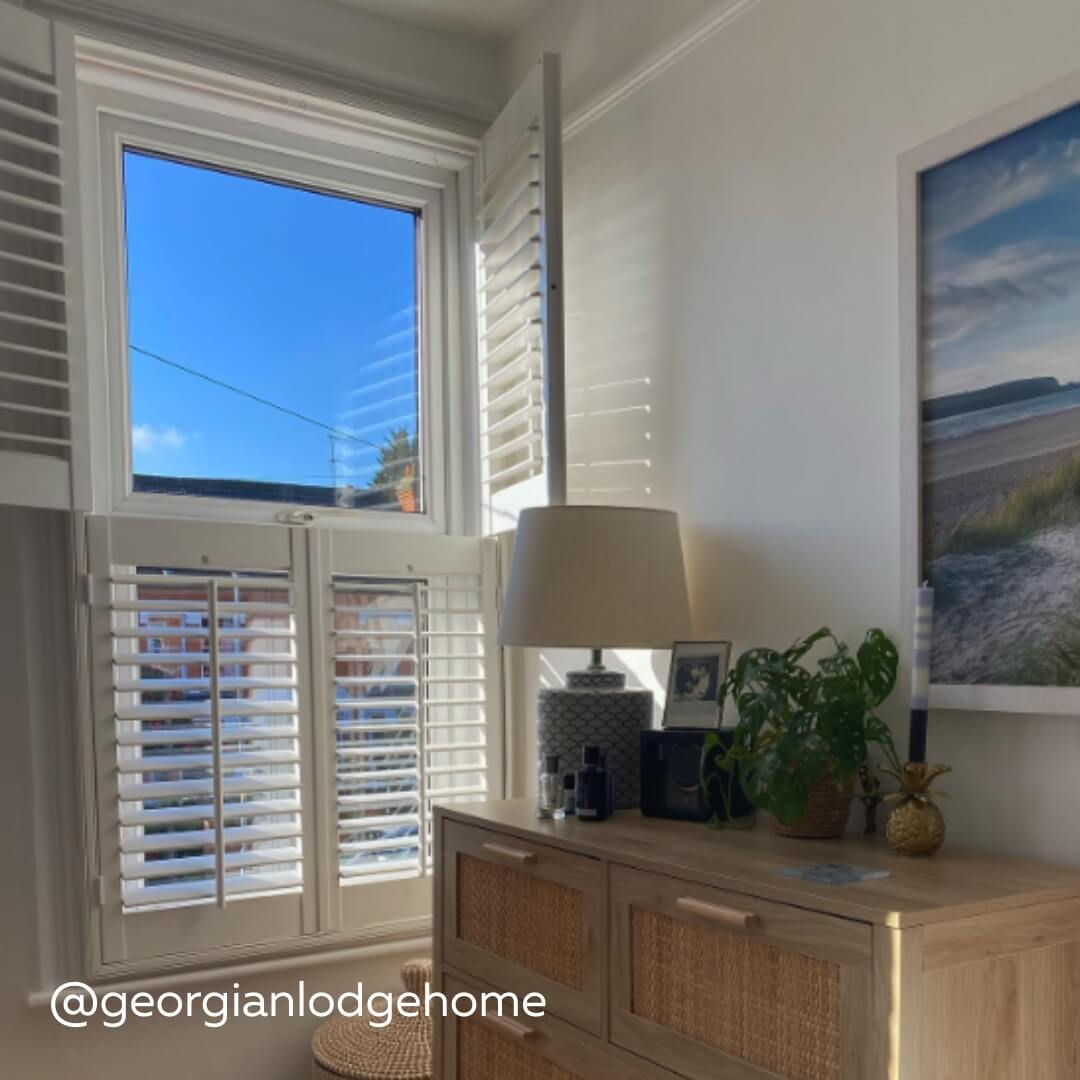 White Tier on Tier Shutters in a modern living room with raffia fronted cupboard and mini monstera